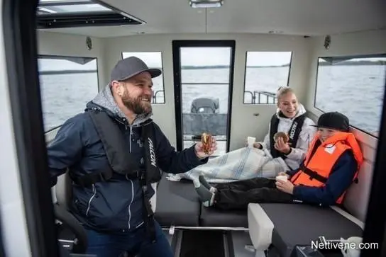 A man in a life jacket enjoys food with two children inside a boat, with large windows showing a water view outside.